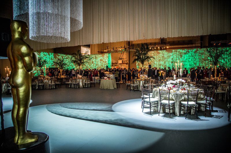 There is a statue of an oscar statue in the middle of a large room with tables and chairs.