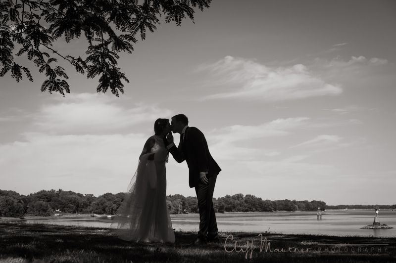 A bride and groom kissing in front of a lake in a black and white photo.