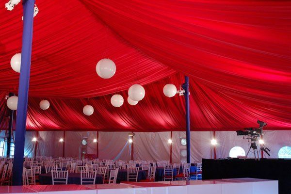 A red and white tent with tables and chairs and lanterns hanging from the ceiling.