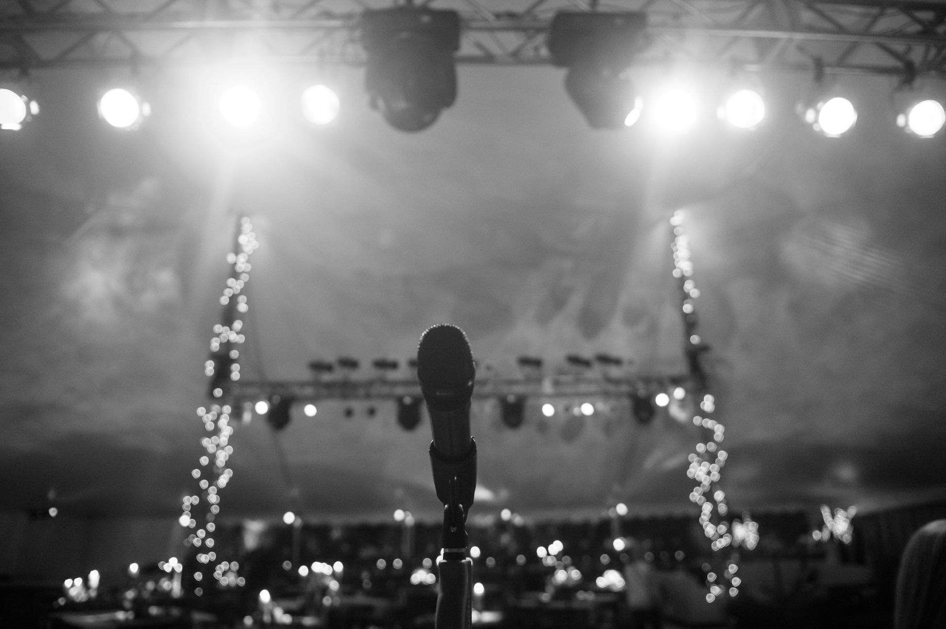 A black and white photo of a microphone in front of a stage with lights.
