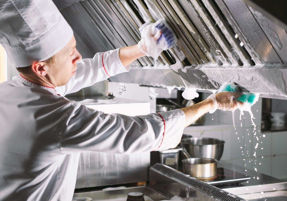 Chef cleaning a commercial kitchen hood