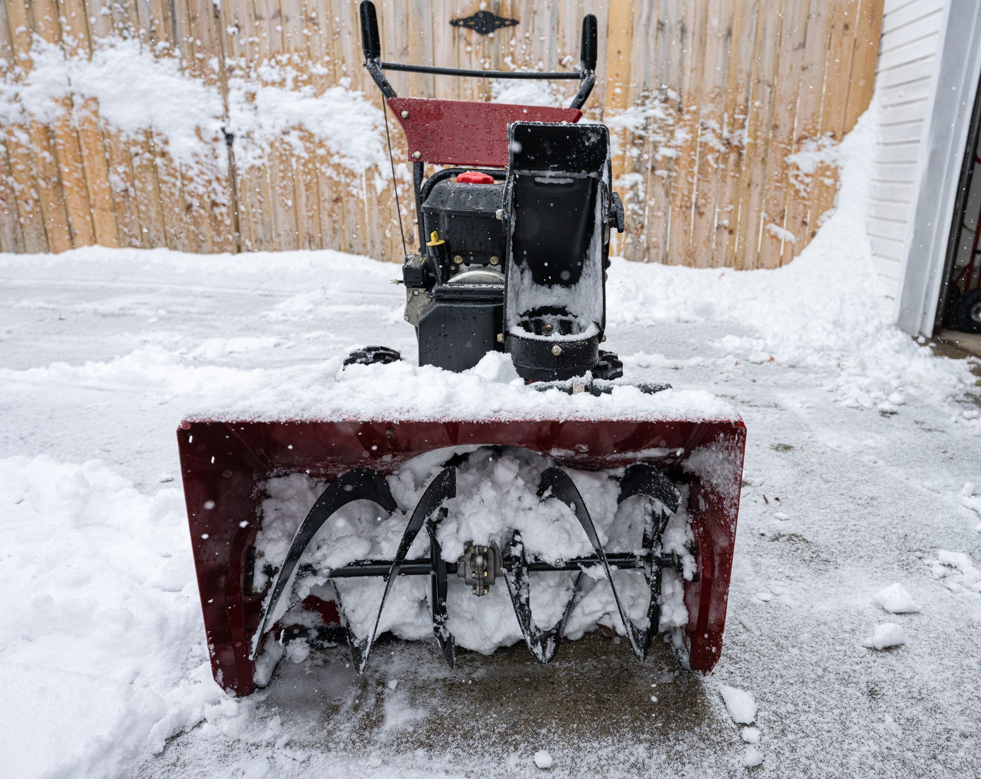Snowblower in a snow-covered area. The machine is red and black, with snow visible inside the auger housing.