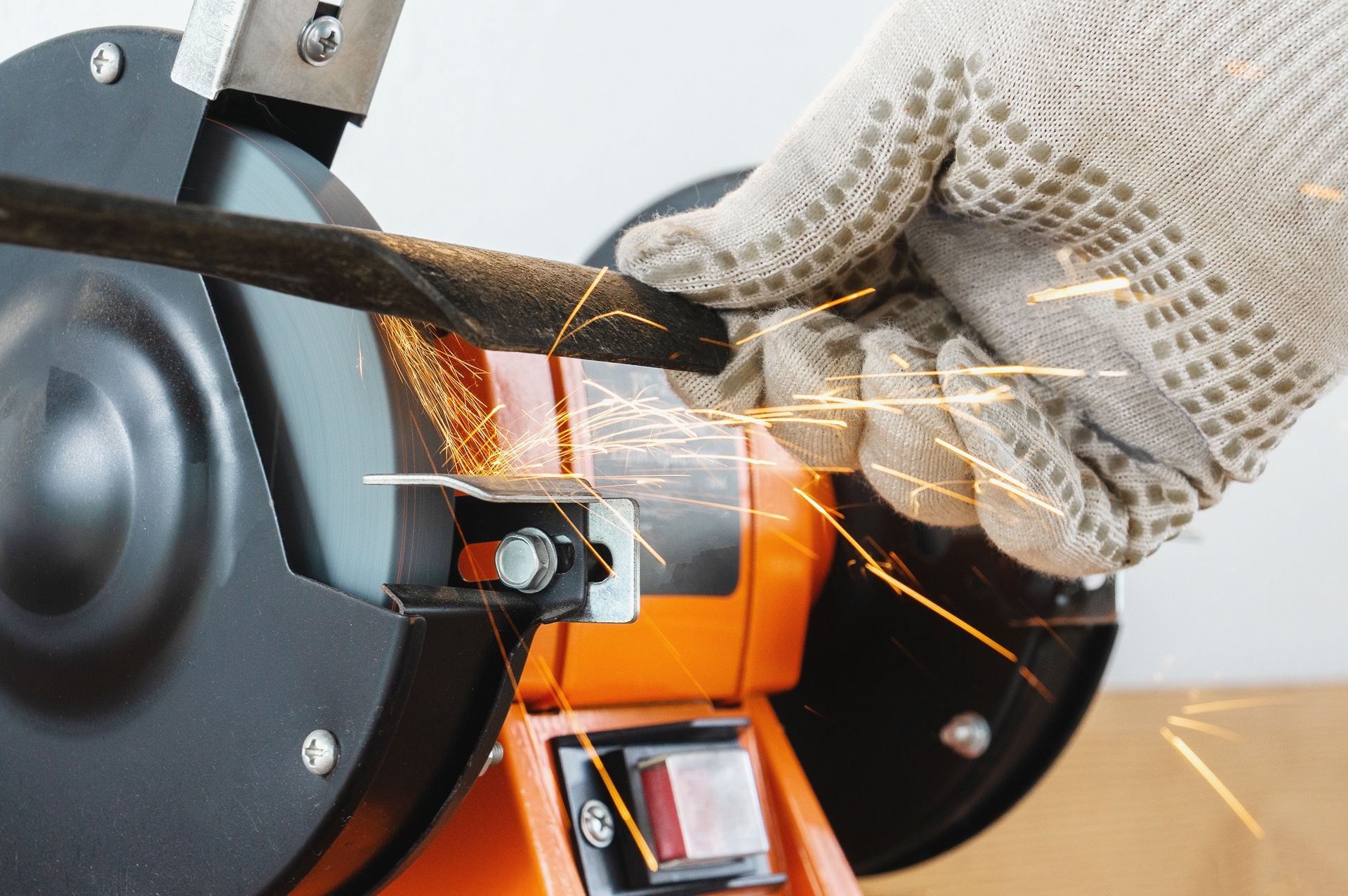 Gloved hand sharpening metal on a grinding wheel, orange and black machine with sparks flying.