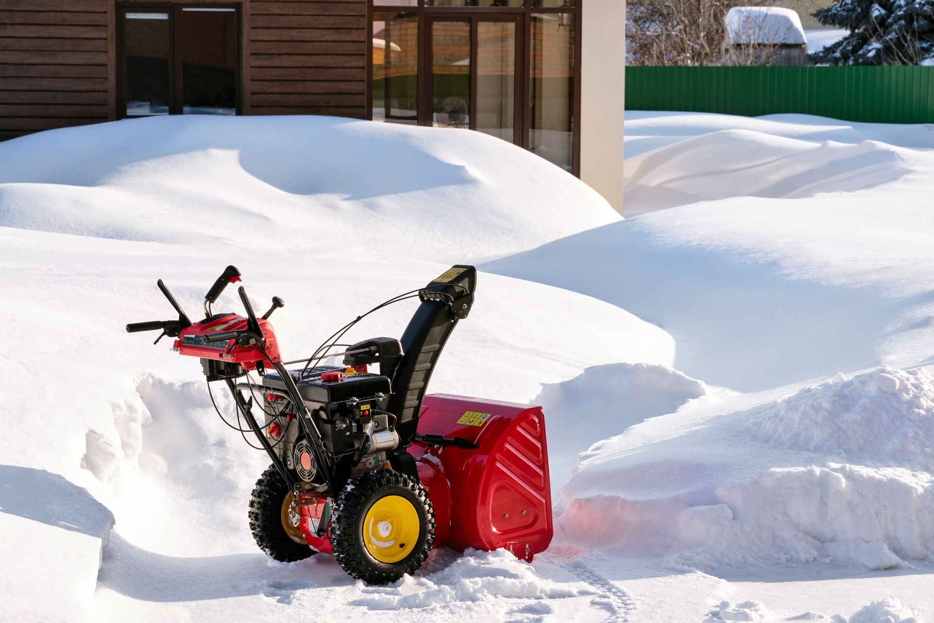 Red snowblower in deep snow next to a house.