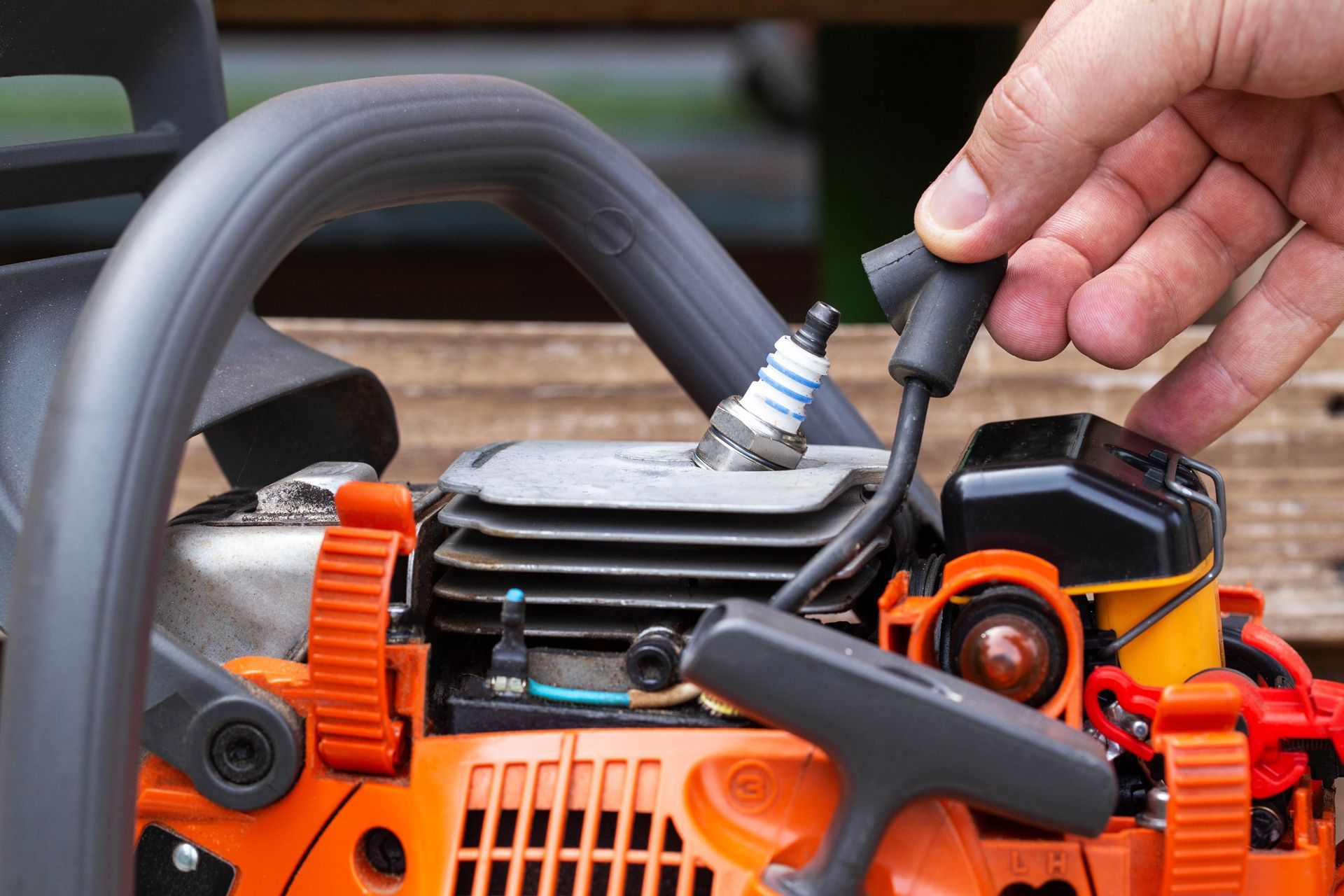 Hand removing spark plug wire from a chainsaw engine.