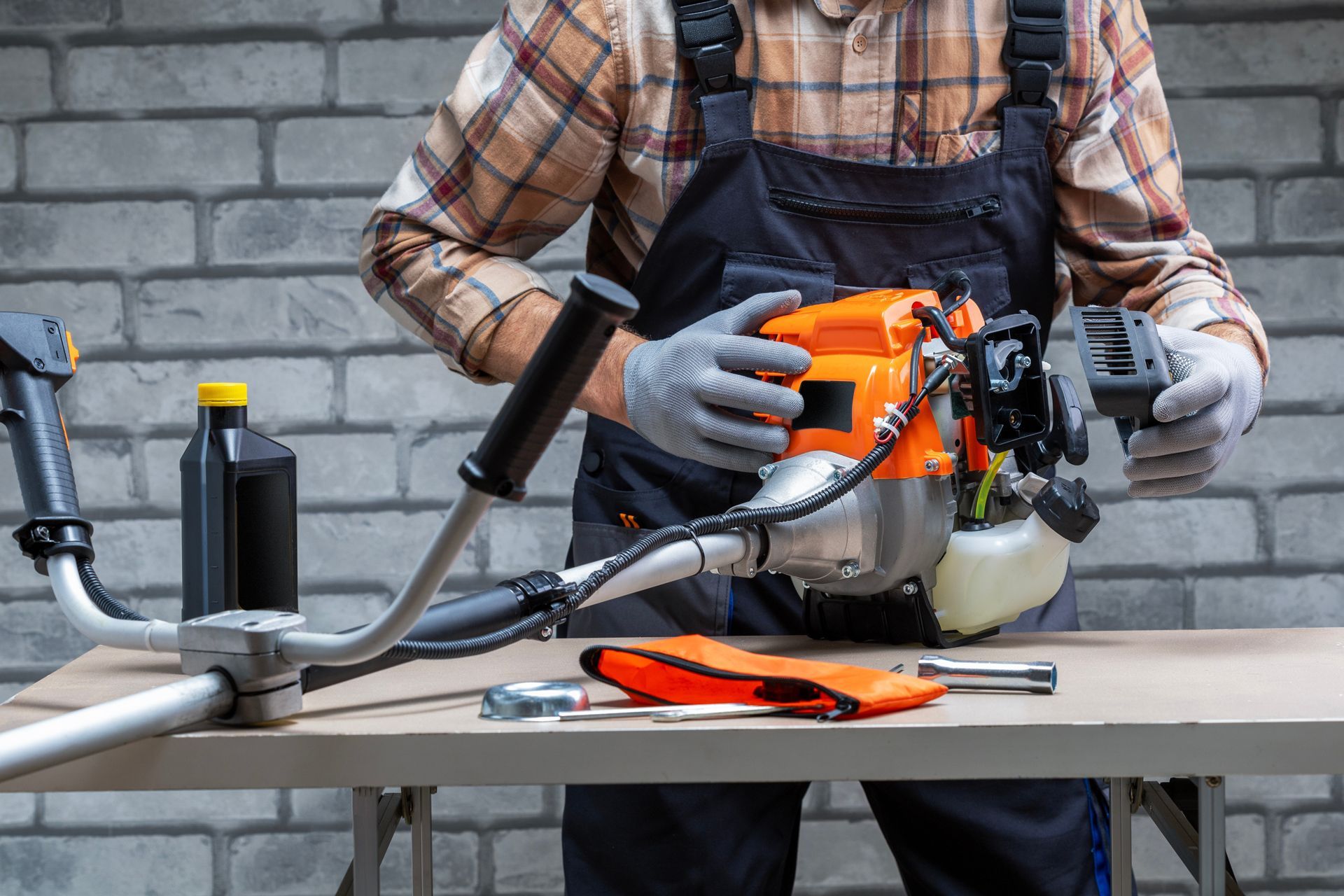 Man in overalls repairs a string trimmer on a workbench.
