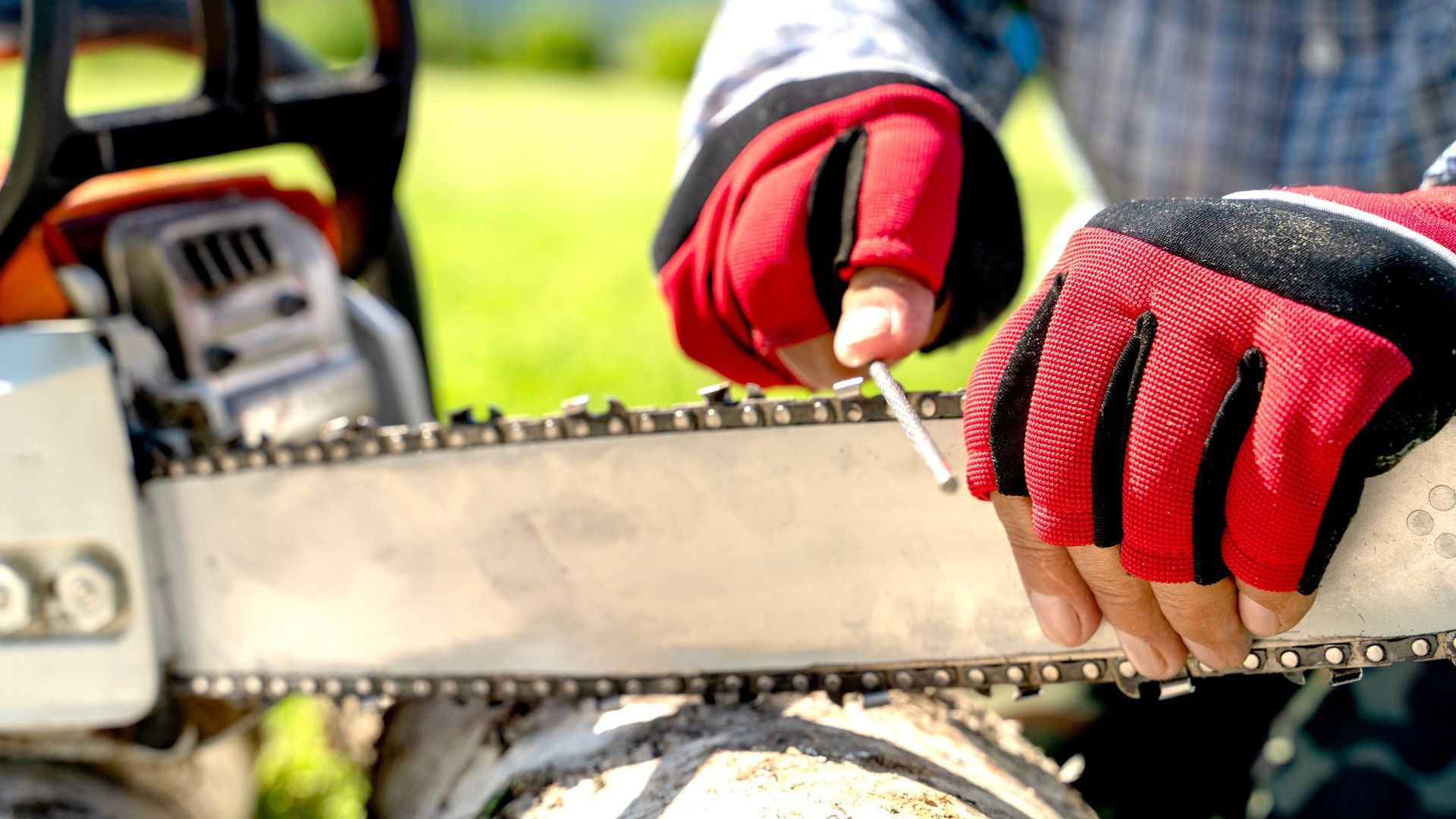 Hands with red work gloves sharpening a chainsaw blade.
