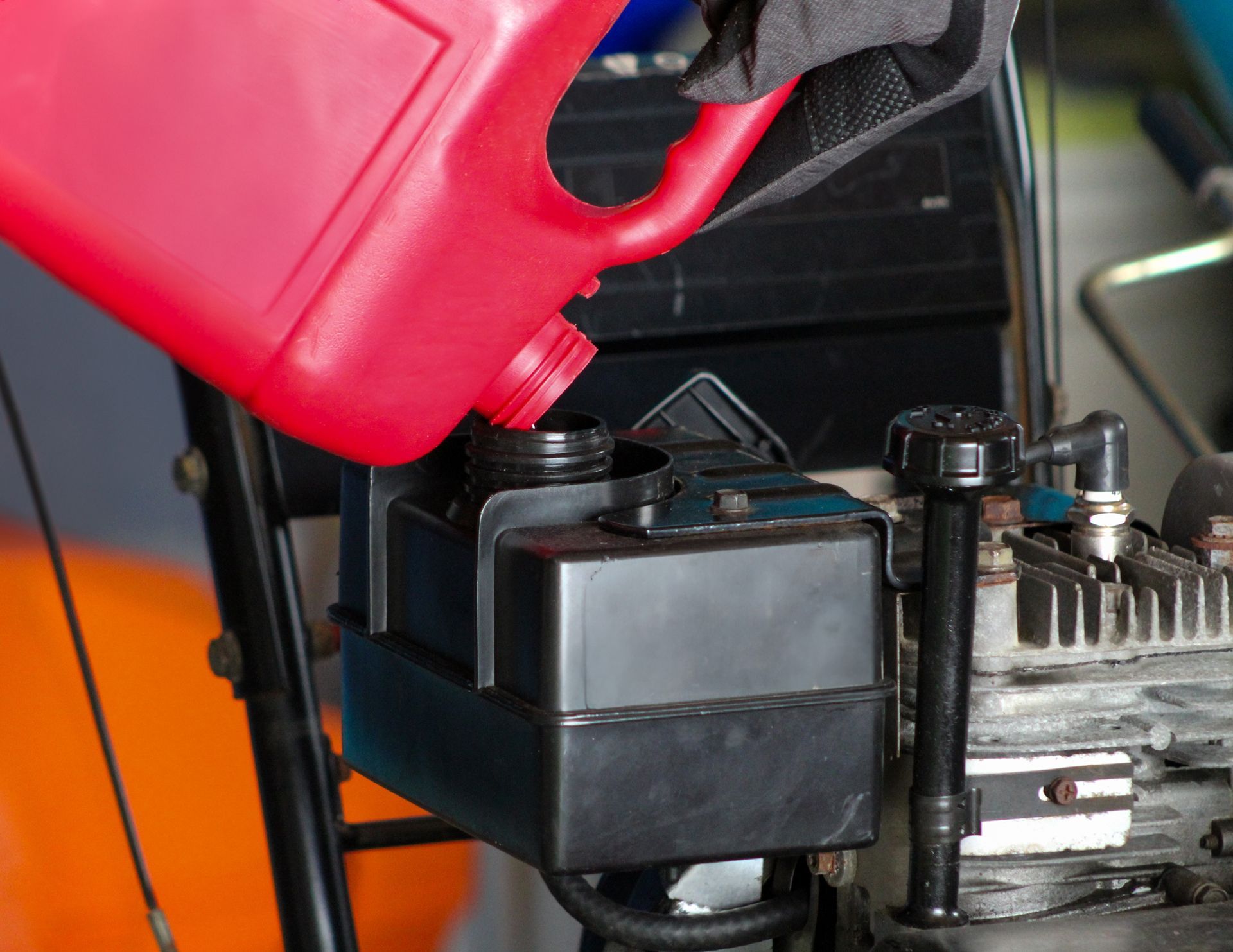 Red gas can pouring fuel into a black engine tank.