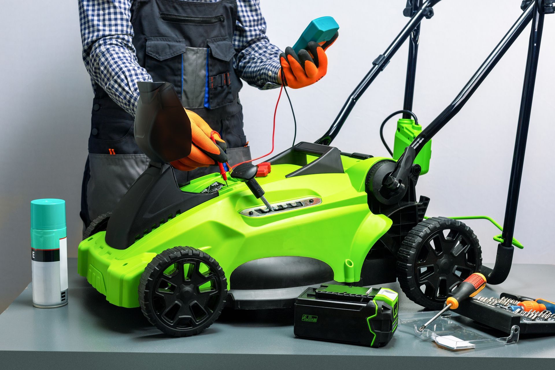 Person testing the electrical system of a green electric lawnmower with a multimeter.
