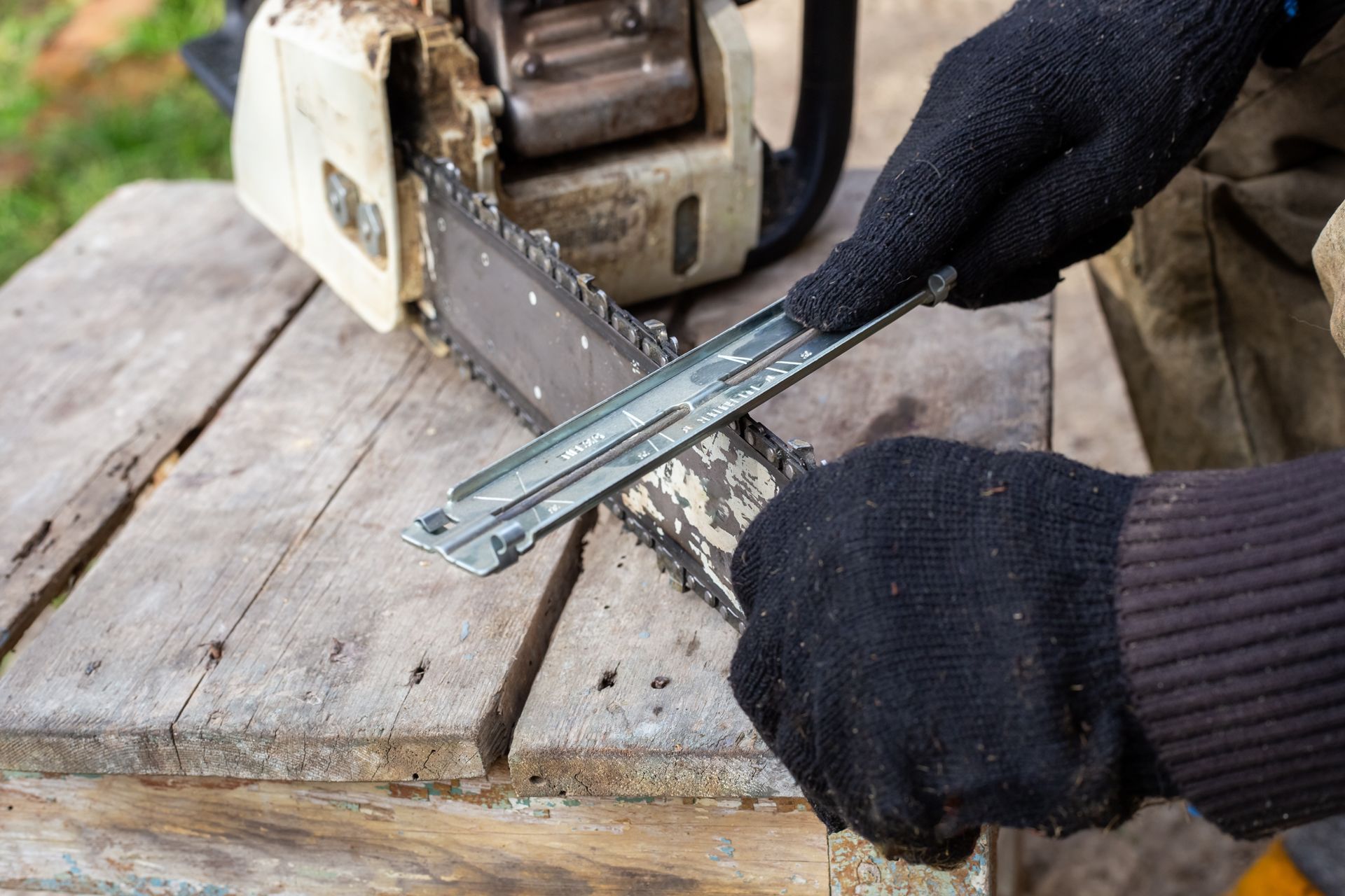 Person sharpening a chainsaw blade with a file while wearing black gloves.