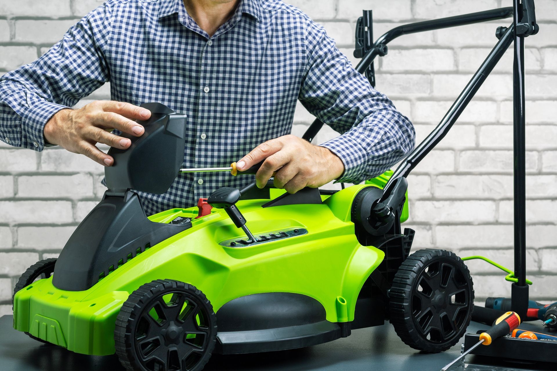 Person using screwdriver to repair a bright green lawn mower on a table indoors.