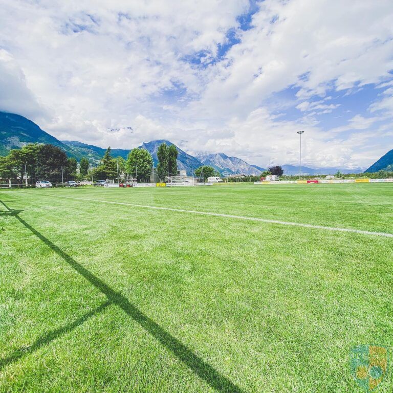 Un terrain de football avec des montagnes en arrière-plan par une journée ensoleillée.