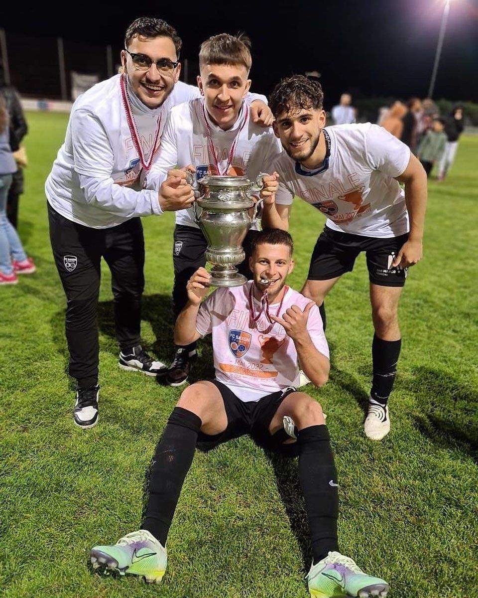 Un groupe de joueurs de football tiennent un trophée sur un terrain.