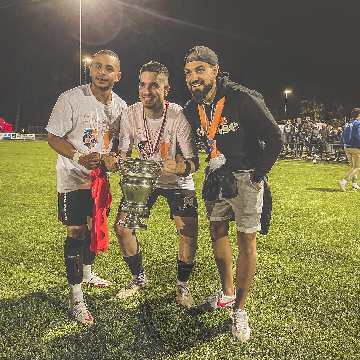 Trois hommes sont debout sur un terrain de football tenant un trophée.