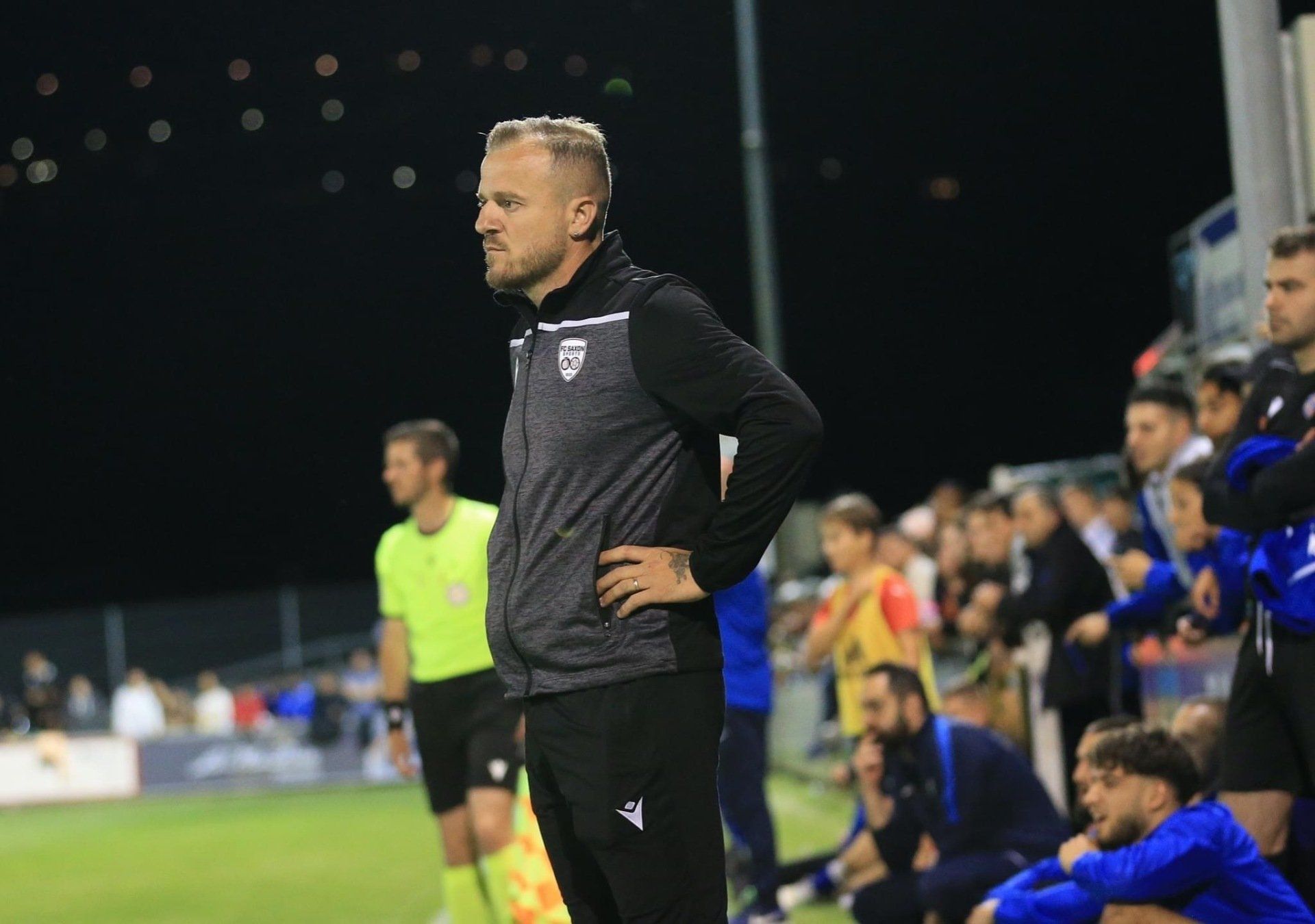 Un homme est debout sur un terrain de football avec ses mains sur ses hanches.