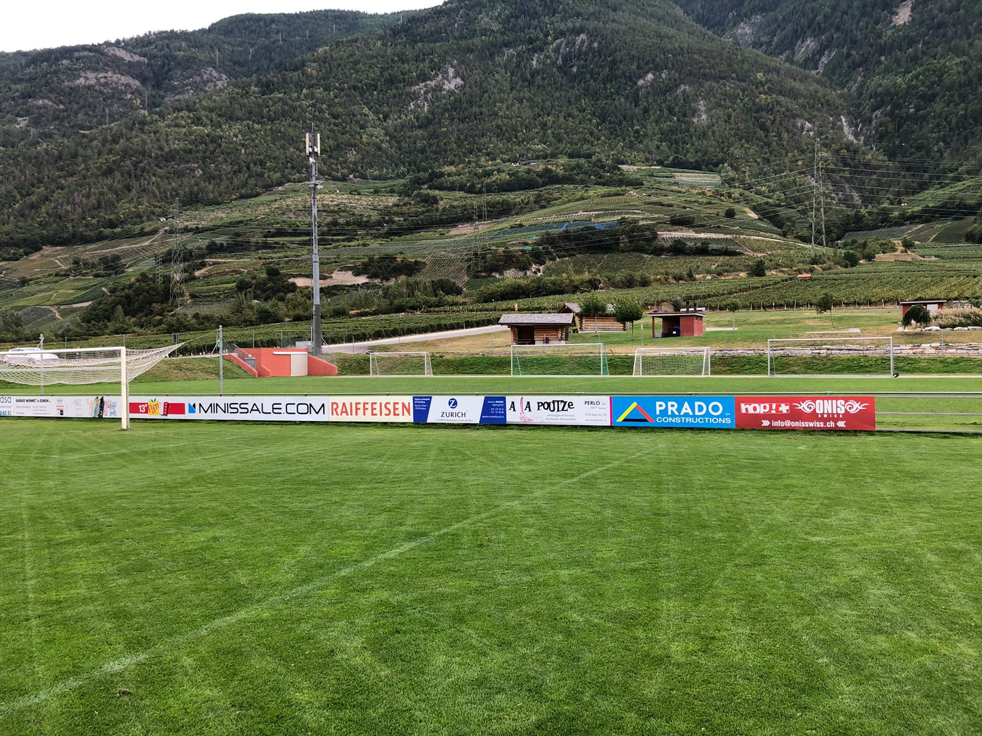 Un terrain de football avec des publicités sur le côté et des montagnes en arrière-plan.