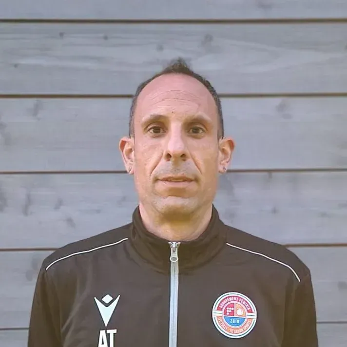 Un homme portant une veste noire se tient devant un mur en bois.