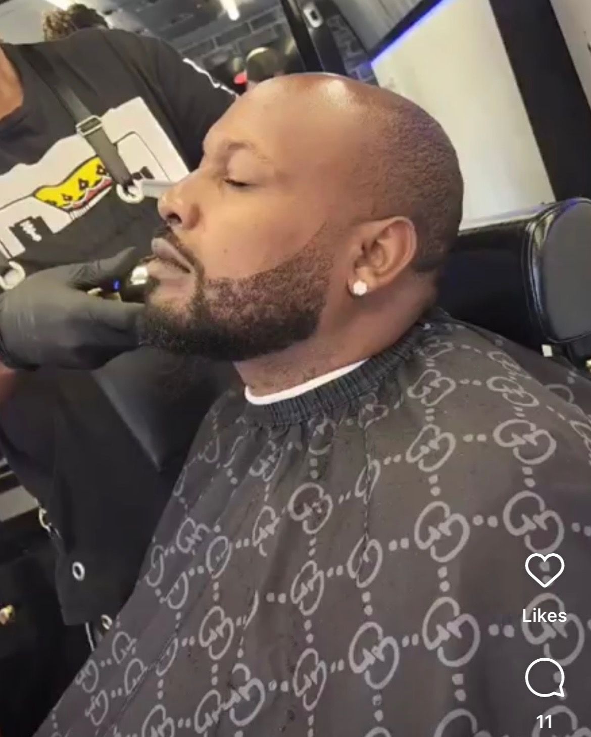 A man is getting his hair cut by a barber wearing a gucci cape