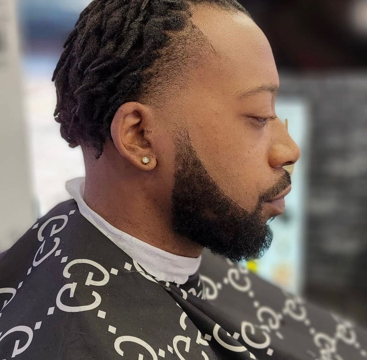 A man with dreadlocks and a beard is getting his hair cut at a barber shop.