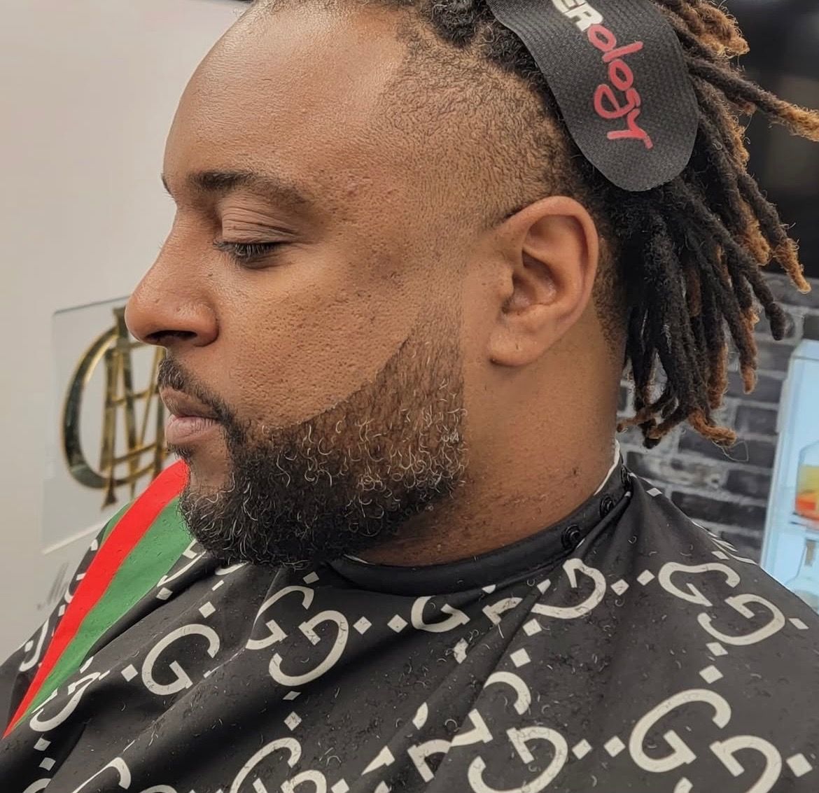 A man with dreadlocks and a beard is getting his hair cut at a barber shop.