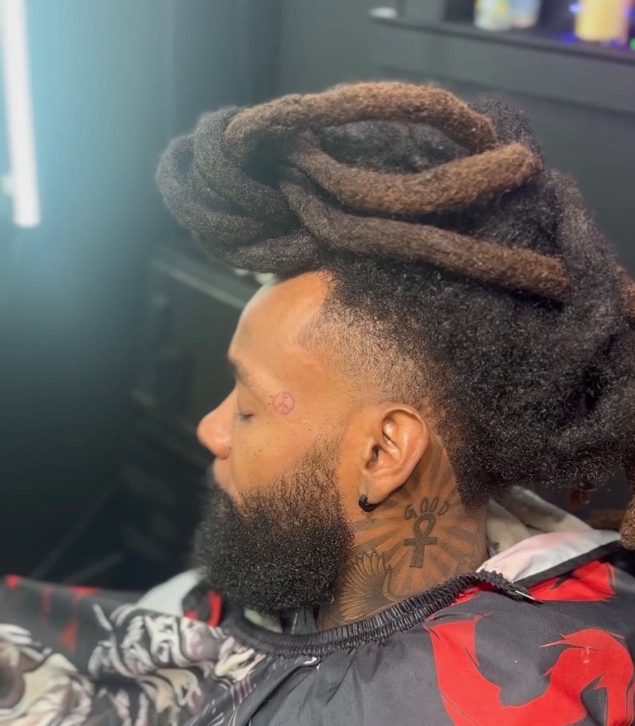 A man with dreadlocks and a beard is sitting in a chair at a barber shop.