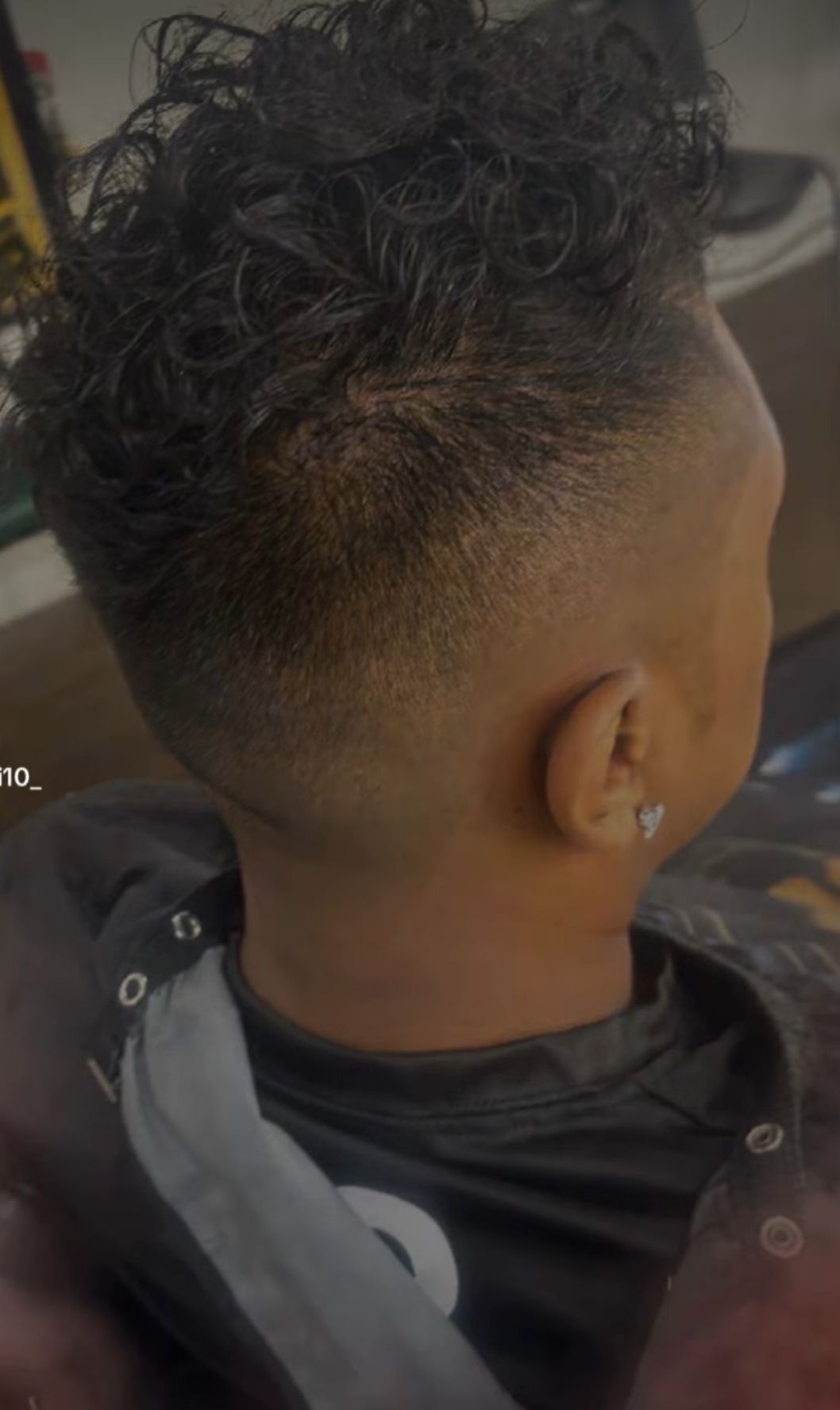 A man with curly hair is getting his hair cut at a barber shop.