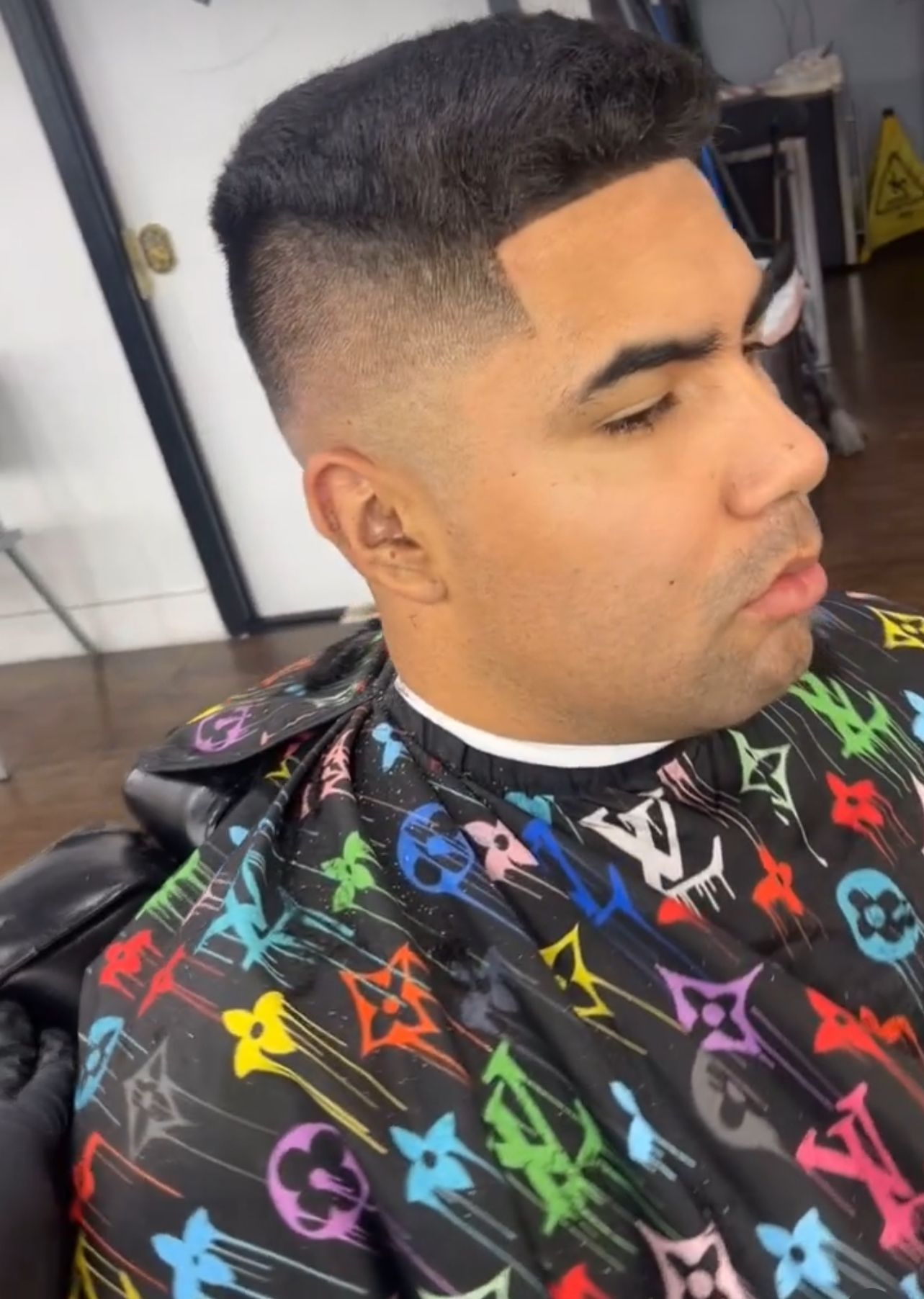 A man is getting his hair cut by a barber wearing a louis vuitton cape.