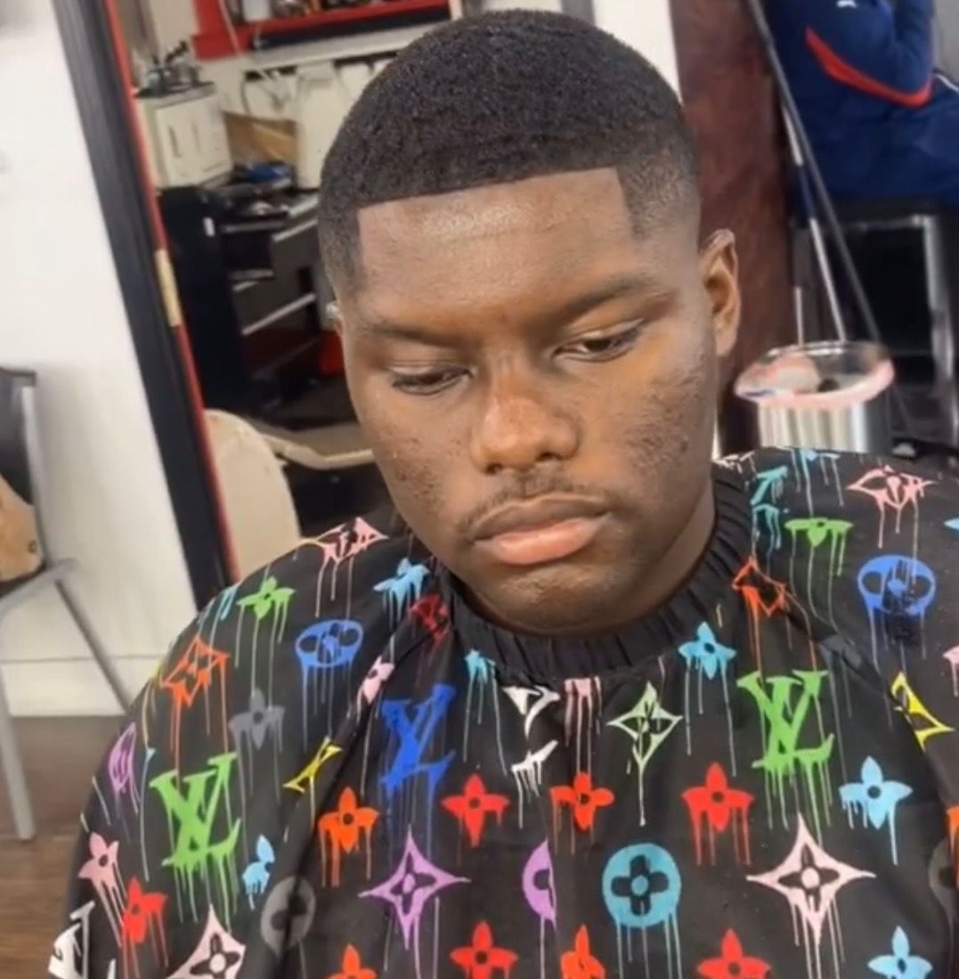 A man wearing a louis vuitton shirt is getting his hair cut