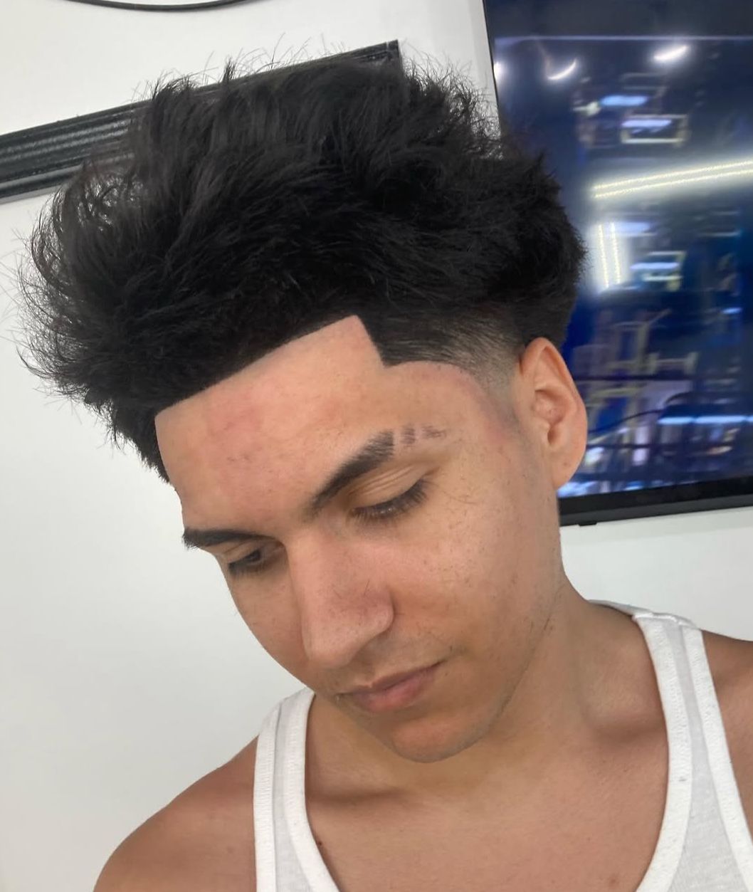 A man with a tattoo on his forehead is wearing a white tank top.