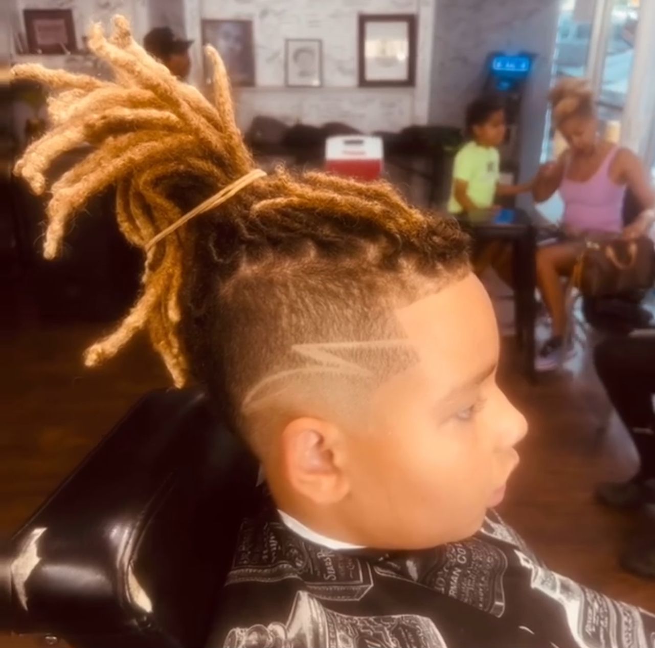 A young boy with dreadlocks is getting his hair cut