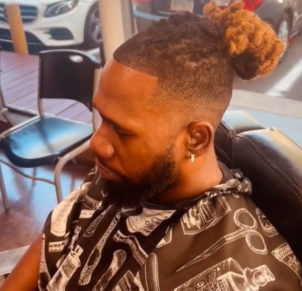 A man is sitting in a chair with a bun in his hair
