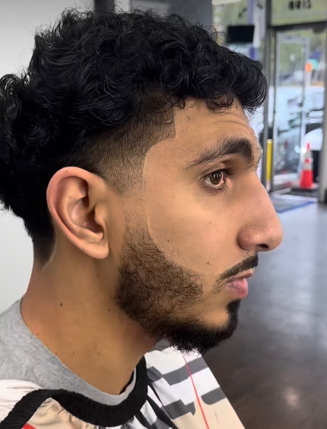 A man with curly hair and a beard is sitting in a barber shop.