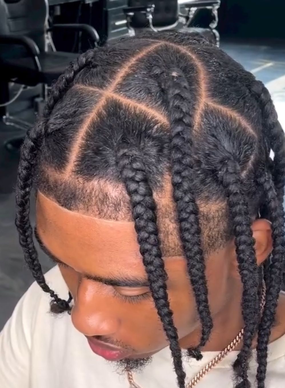 A man with braids in his hair is wearing a white shirt and a gold chain.