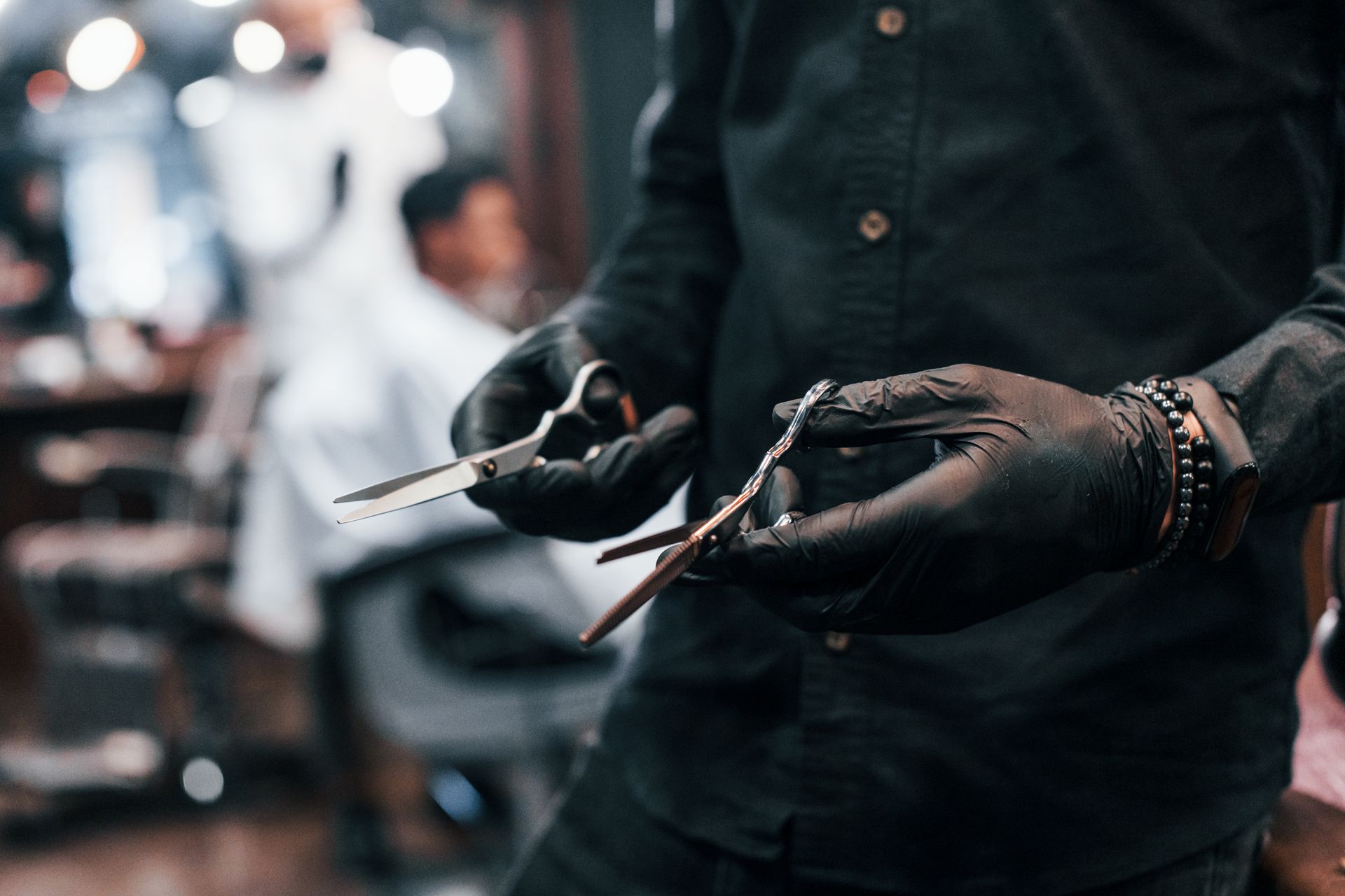 A barber wearing black gloves is holding a pair of scissors in his hands.