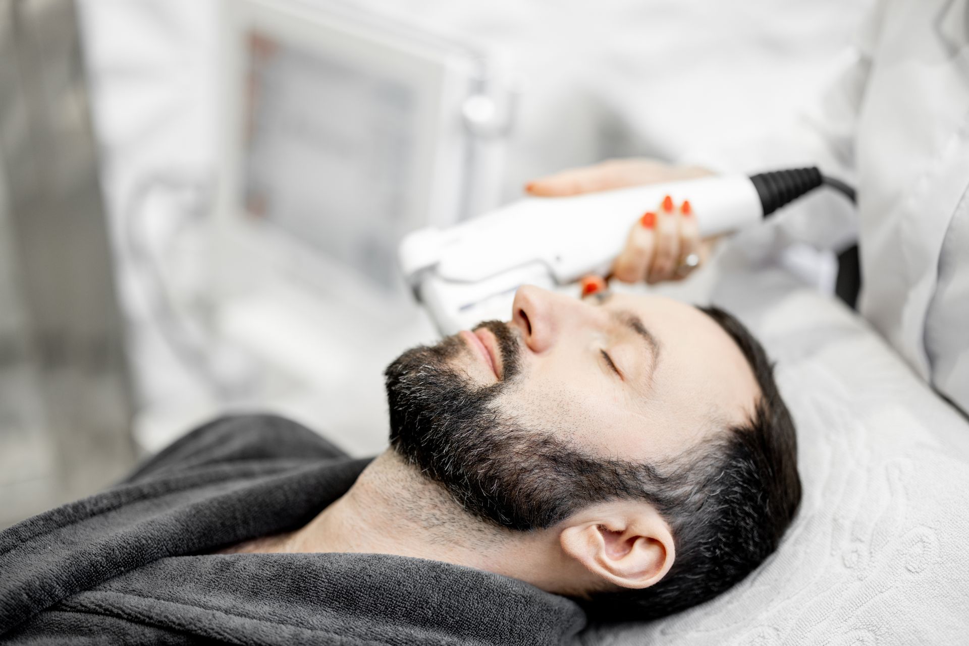 A man with a beard is getting a laser treatment on his face.