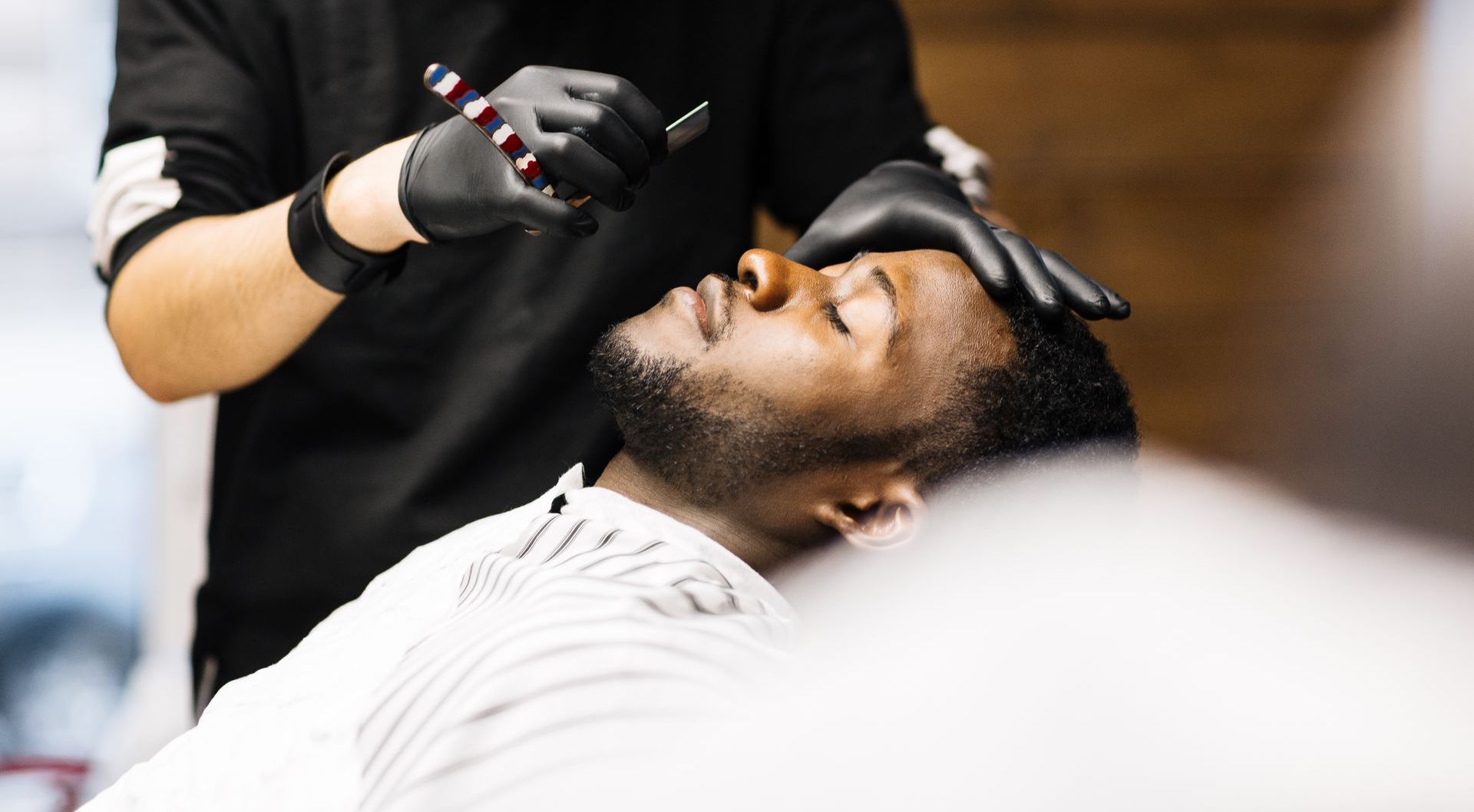 A man is getting his beard shaved by a barber in a barber shop.