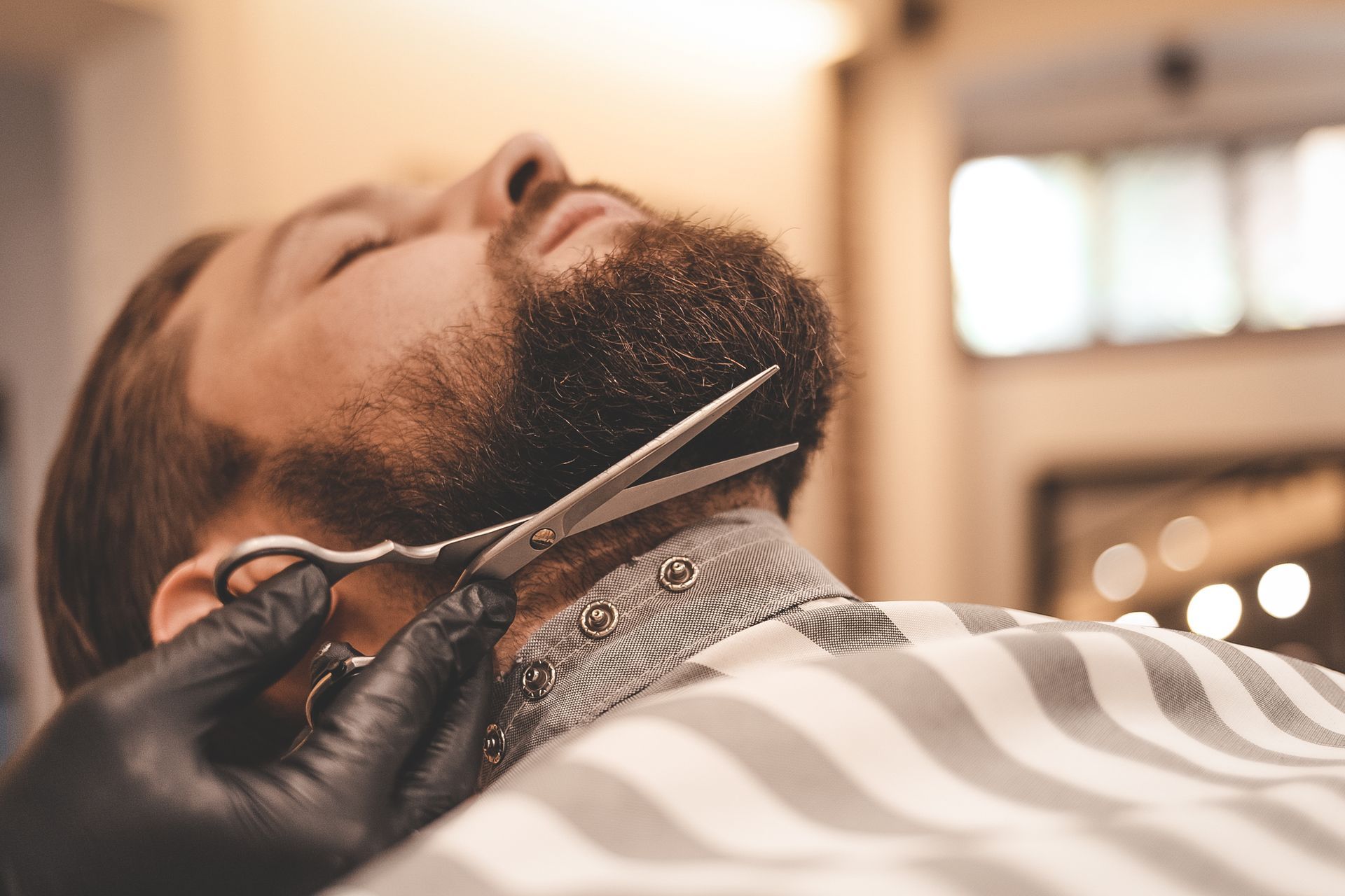 A man is getting his beard cut by a barber with scissors.