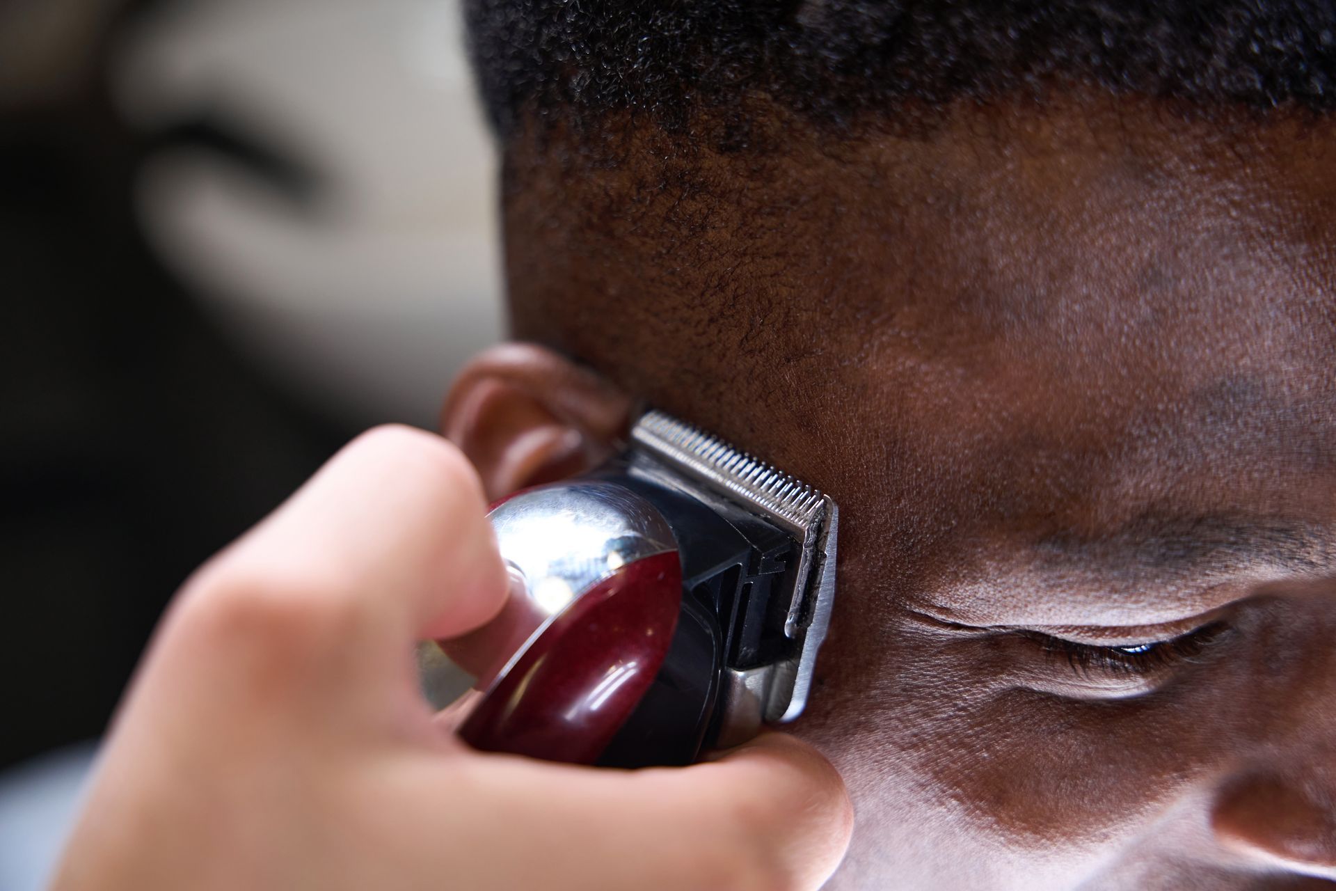 A man is getting his hair cut by a barber with a clipper.