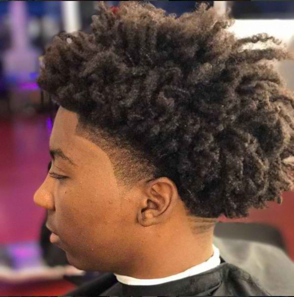 A young man with curly hair is getting his hair cut at a barber shop.
