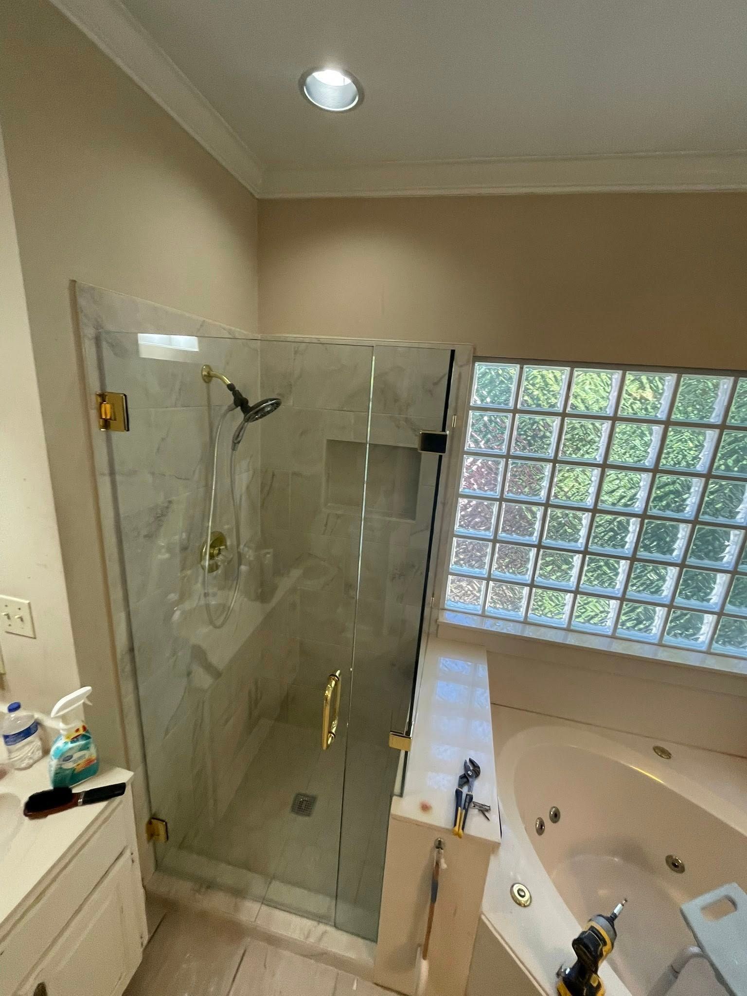 Bathroom with glass shower, gold fixtures, and a glass block window next to a jacuzzi tub.