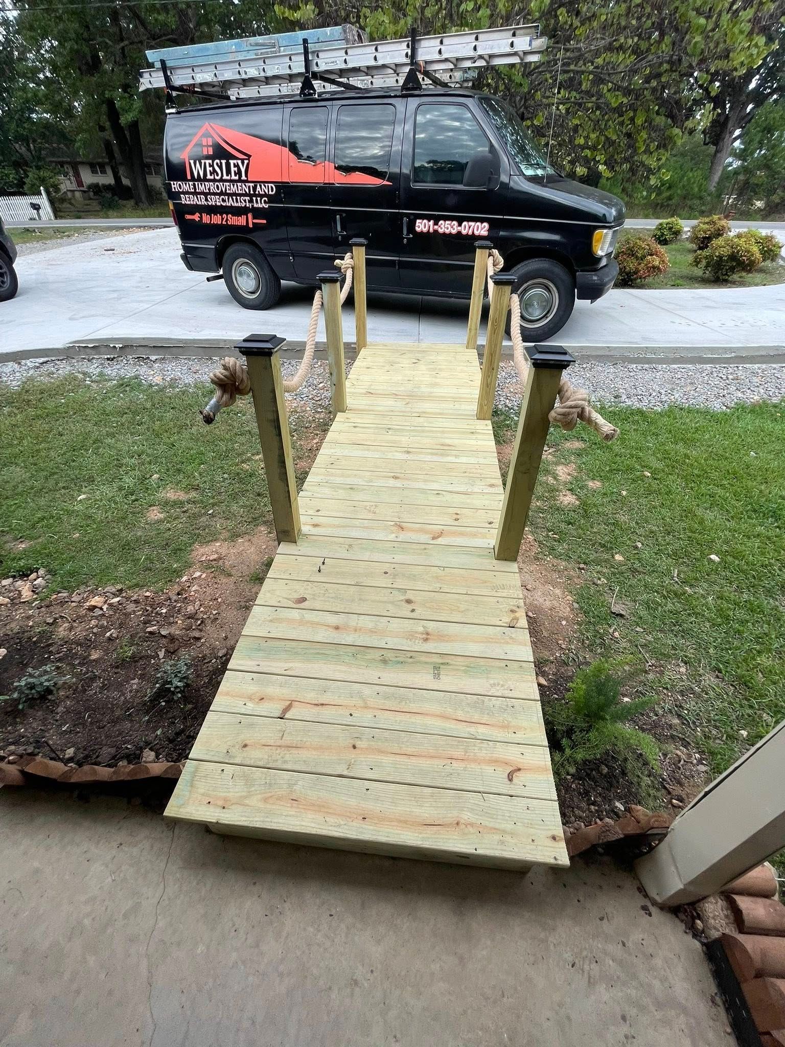 Wooden ramp bridge over a small ditch with a black van parked behind it.