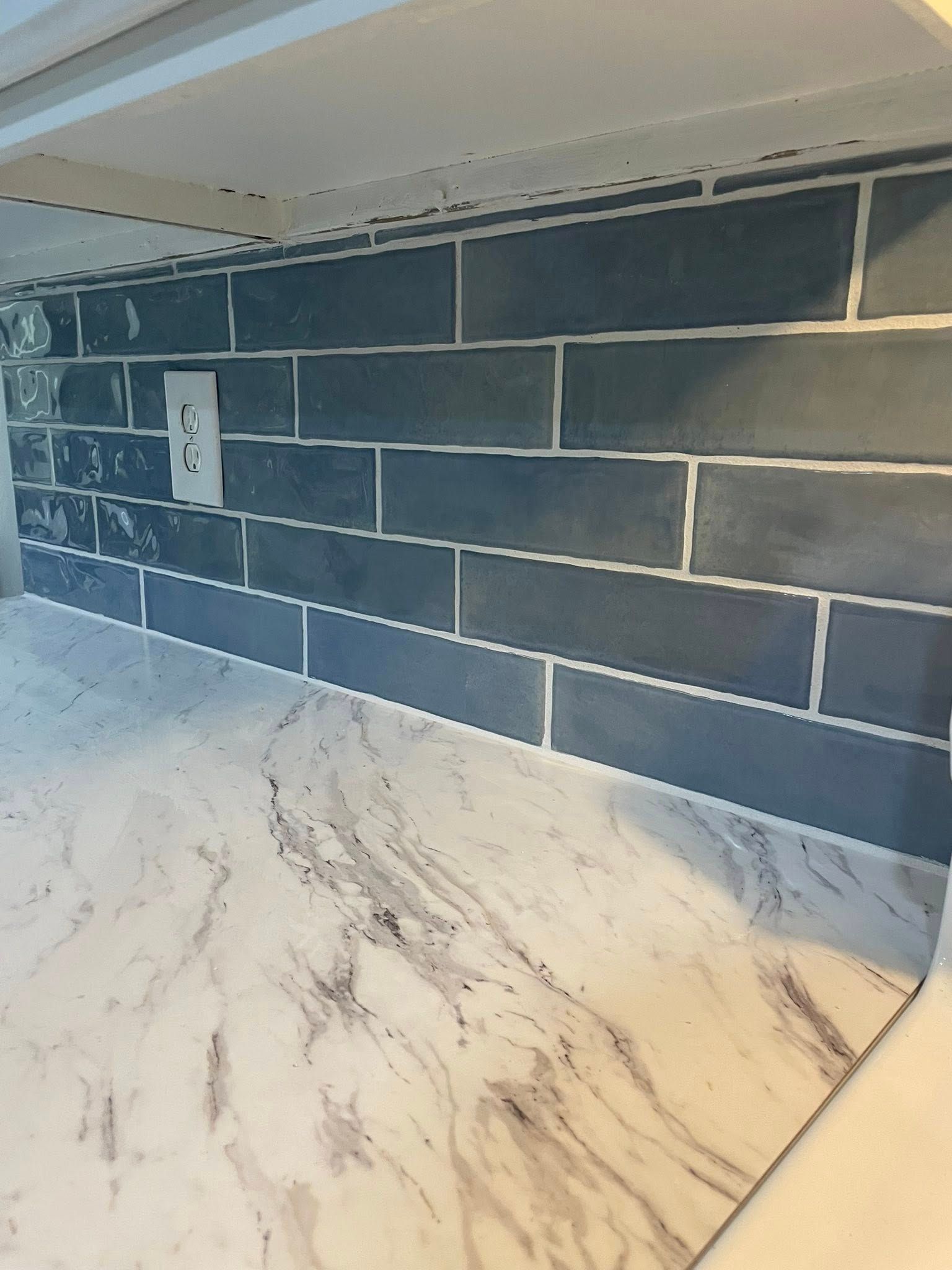 Kitchen backsplash with gray rectangular tiles, white grout, and marble-look countertop.