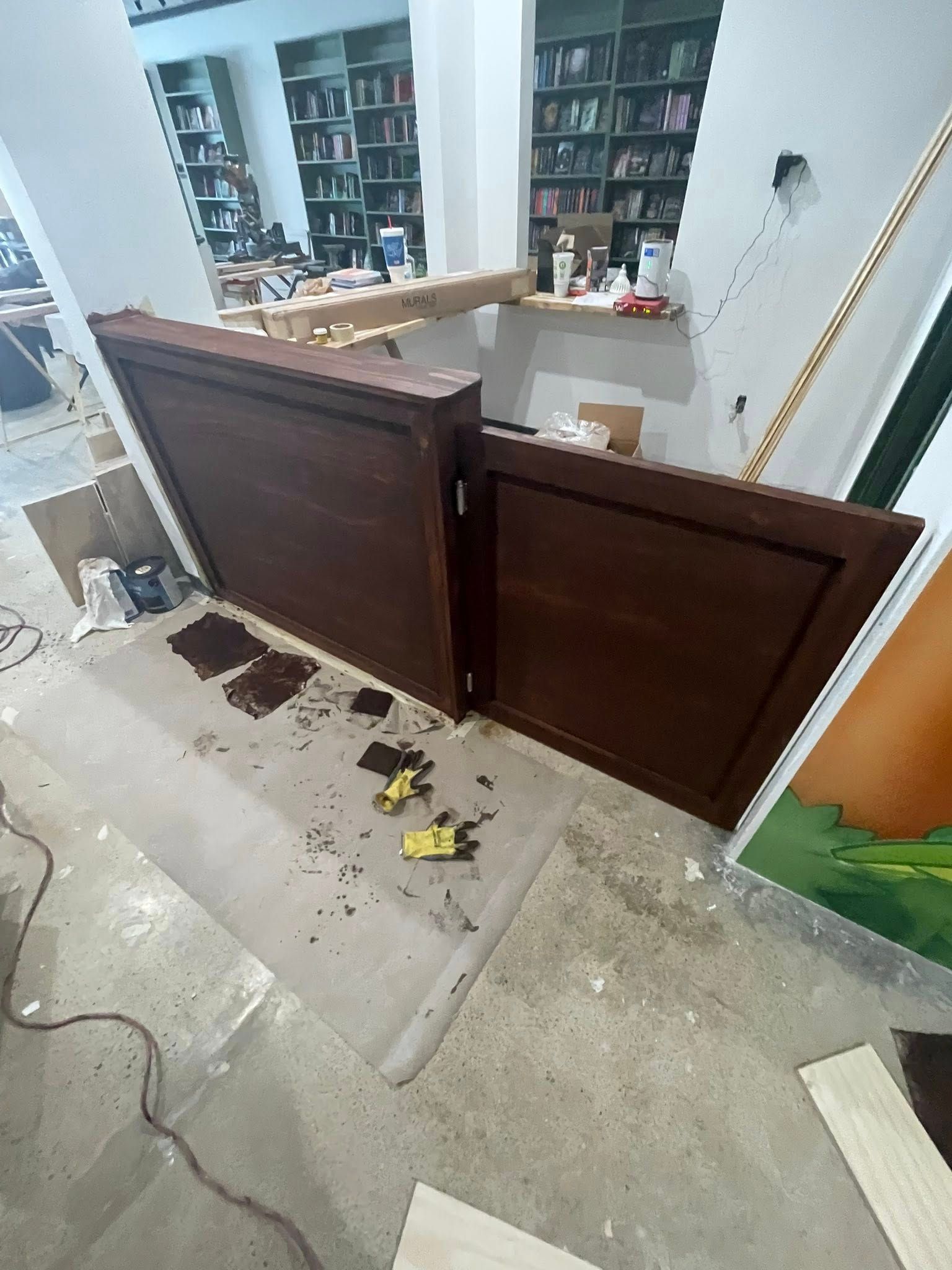 Two dark brown wooden doors, partially open, against a wall. Construction debris on the floor.