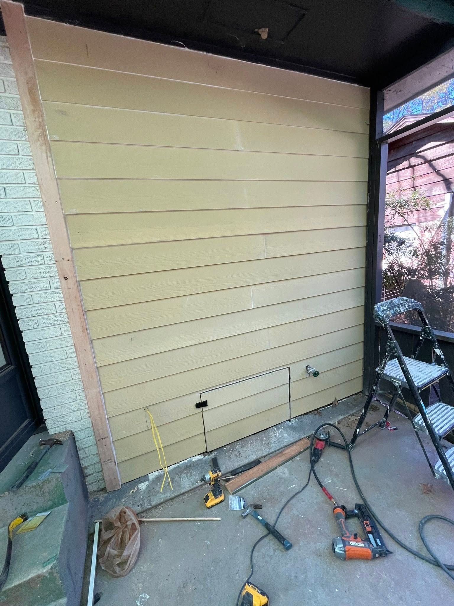 Wall with siding being installed; tools on the ground.