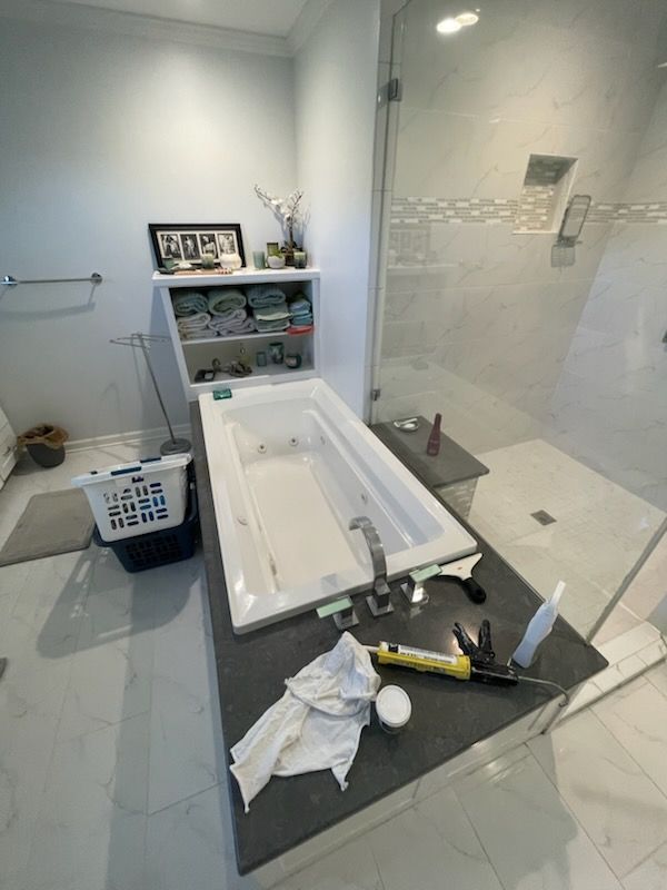 Bathroom with white tub, dark countertop, and glass shower. Tools and supplies on the countertop. Shelves with towels above tub.