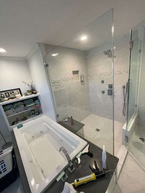 Bathroom with glass shower, bathtub, and shelves. White and gray tiled walls.