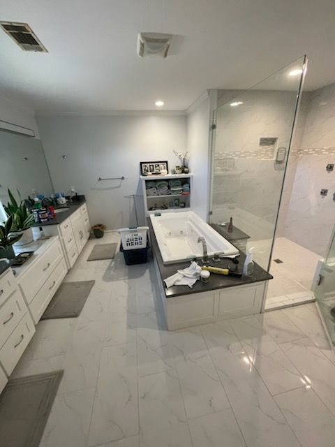Bathroom with white cabinets, tub, and glass shower; gray countertops and white tile floors.