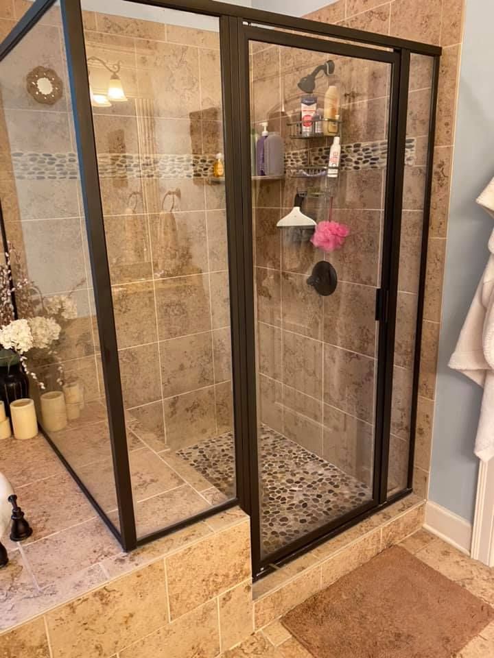 Shower with brown tiles, pebbled floor, glass doors, and dark frame.