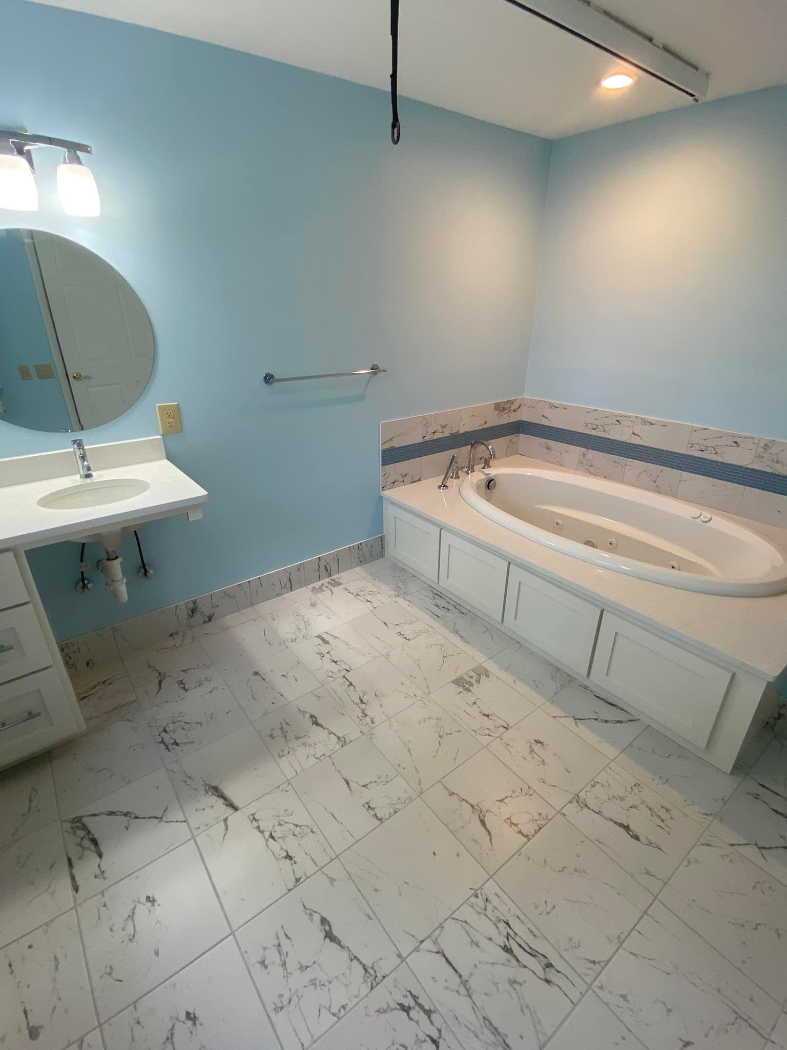 Bathroom with blue walls, white marble-look floor and vanity, oval bathtub with built-in cabinetry.
