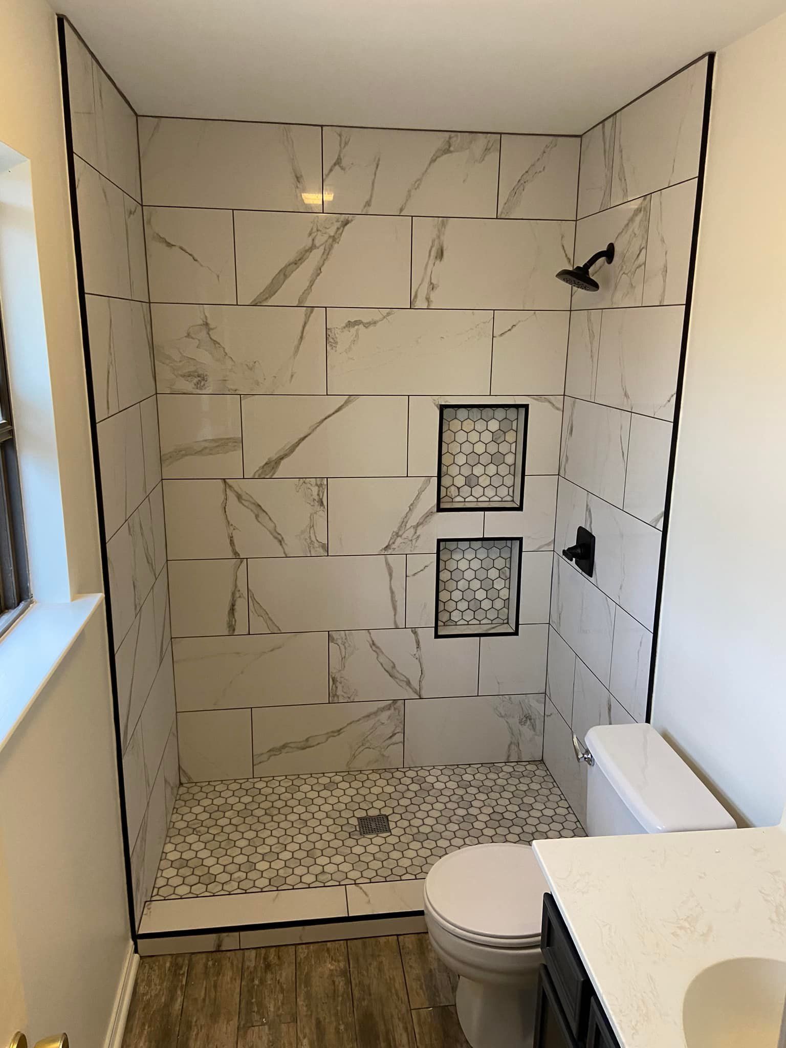 A renovated bathroom with white marble tile shower, black fixtures, and a toilet.